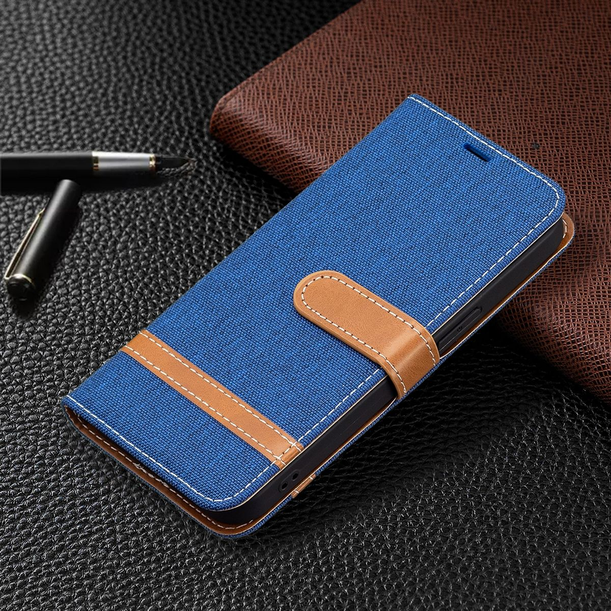 Blaue Handyhülle mit braunem Streifen und Nähten. Stift liegt auf Leder neben der Hülle.