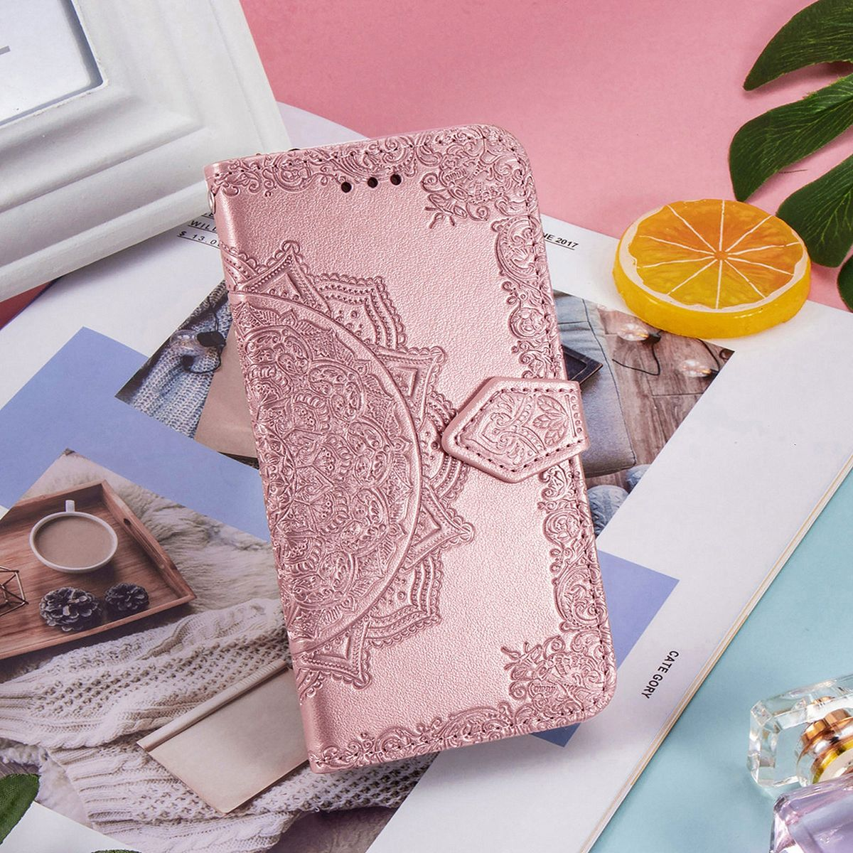Rosa Handyhülle mit aufwendigem Design, auf einem Magazin liegend, mit Zitrone und Blättern.