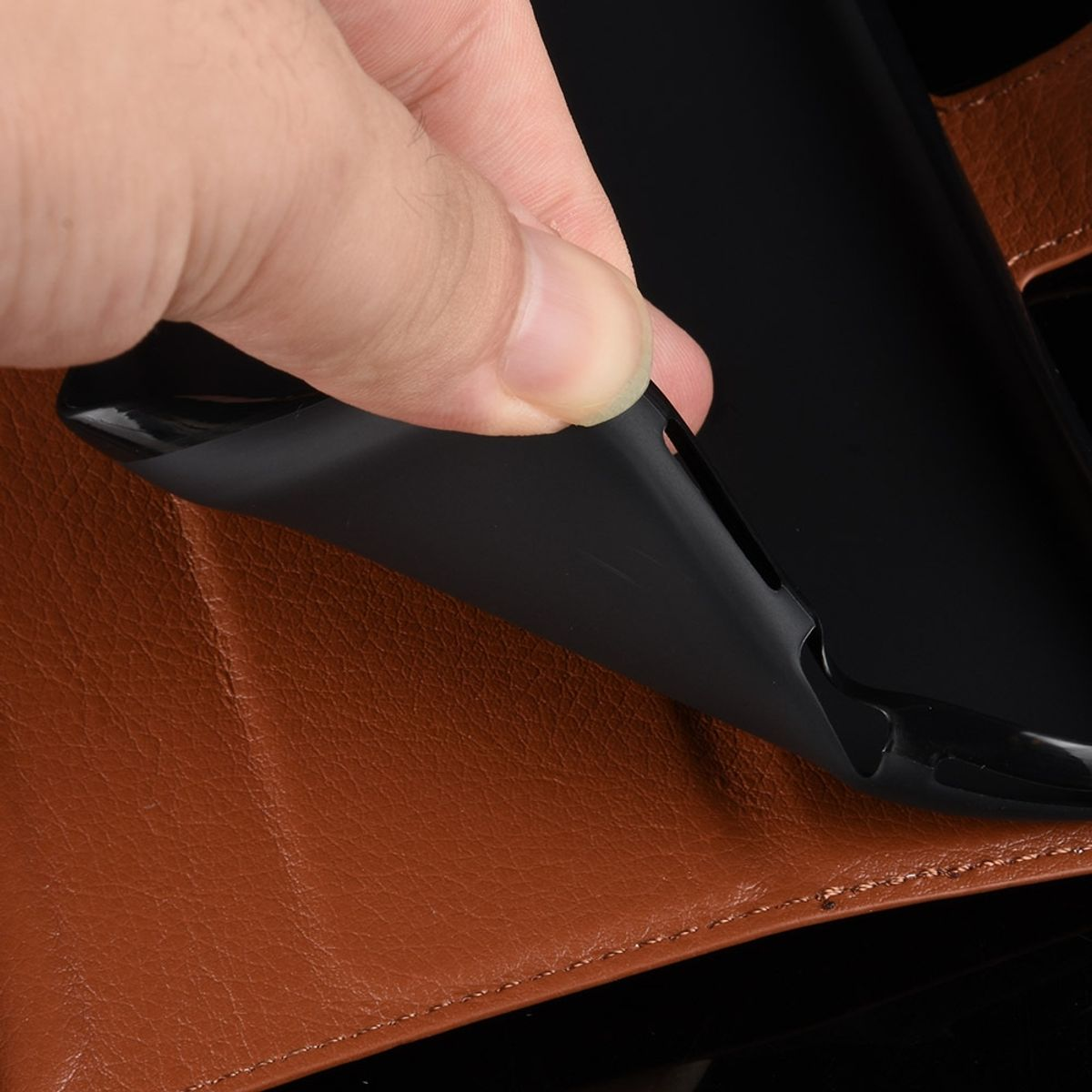 Eine Hand, die eine schwarze Handyhülle von einer braunen Leder-Handyhülle abzieht.