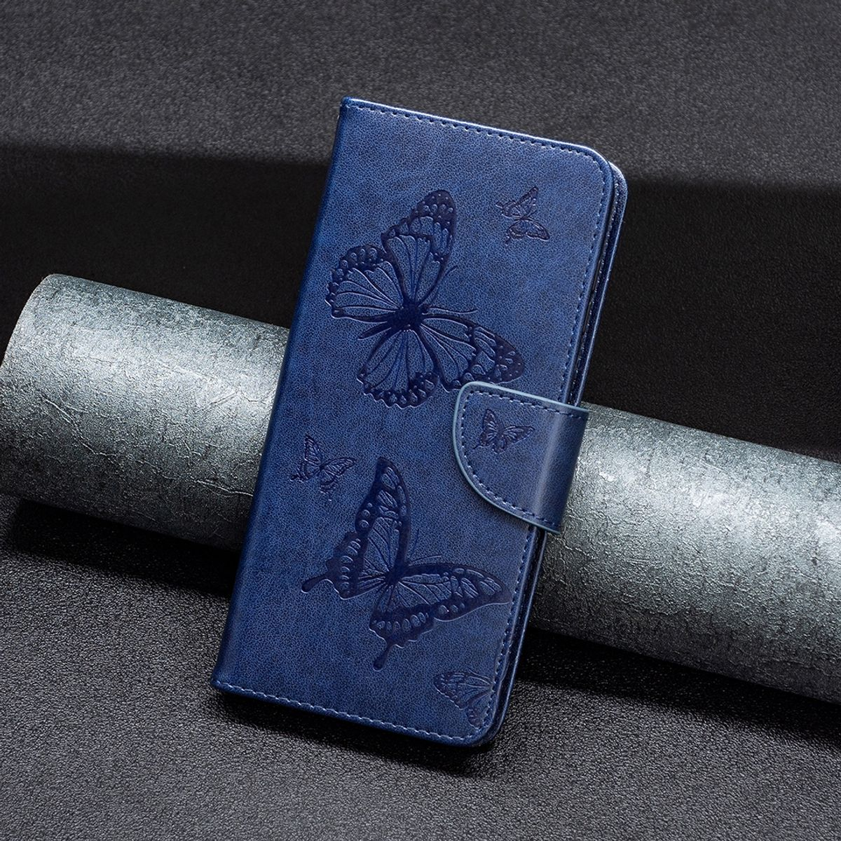 Eine blaue Handyhülle mit Schmetterlingsprägungen, mit einem Verschluss geschlossen, auf dunkler Oberfläche.