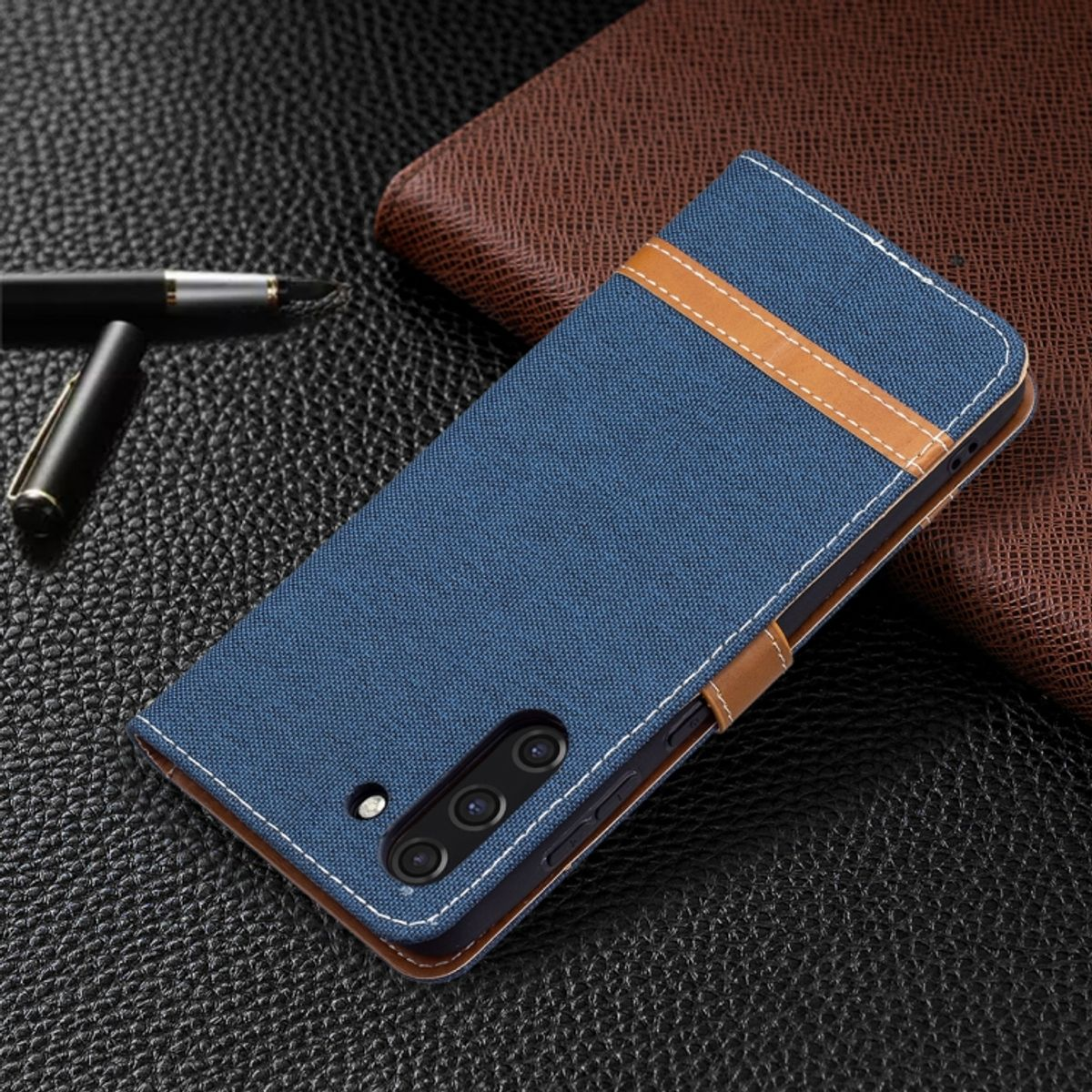 Blaue Handyhülle mit braunen Lederakzenten. Telefon ist innen. Hülle auf dunkler Oberfläche.