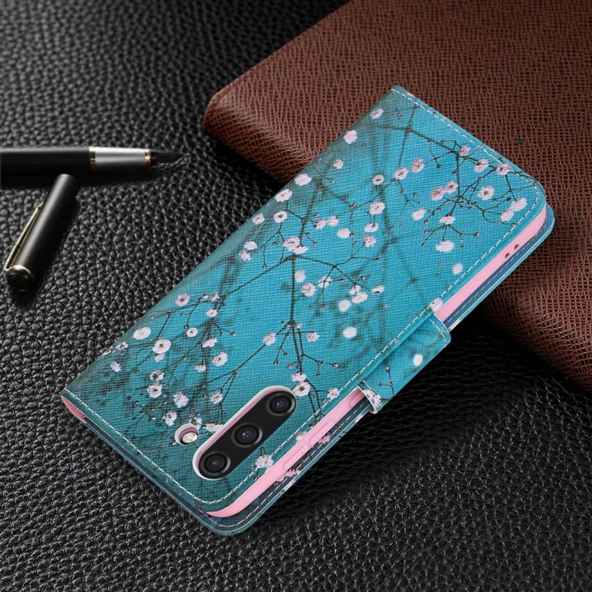 Blaue Handyhülle mit weißem Blumendesign, Stift auf Lederoberfläche.