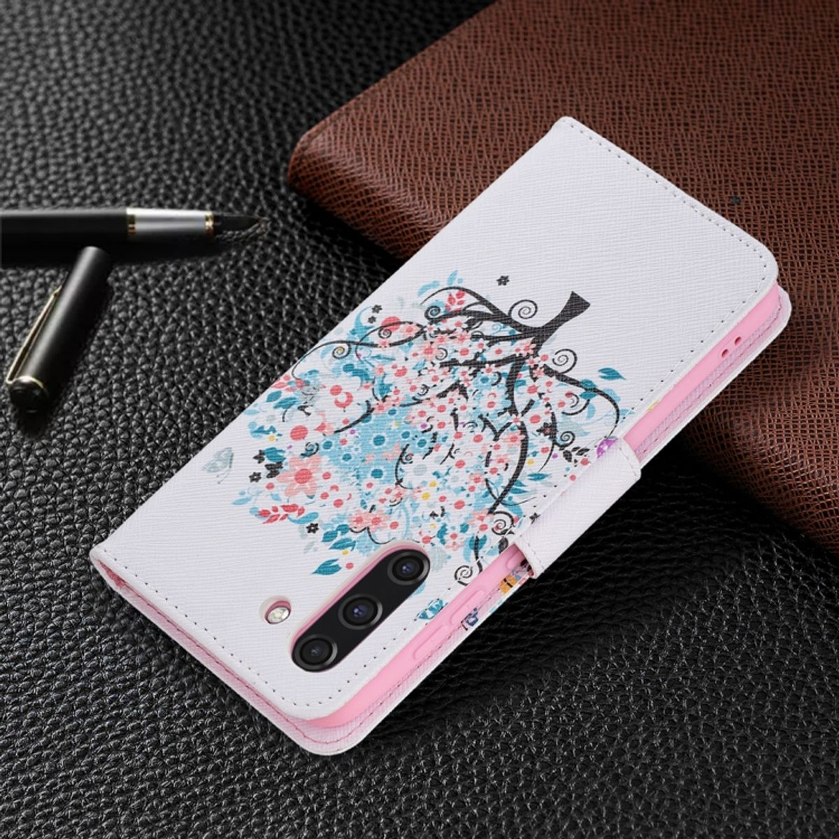 Weiße Handyhülle mit Blumendesign auf strukturierter Oberfläche, mit Stift und braunem Objekt im Hintergrund.