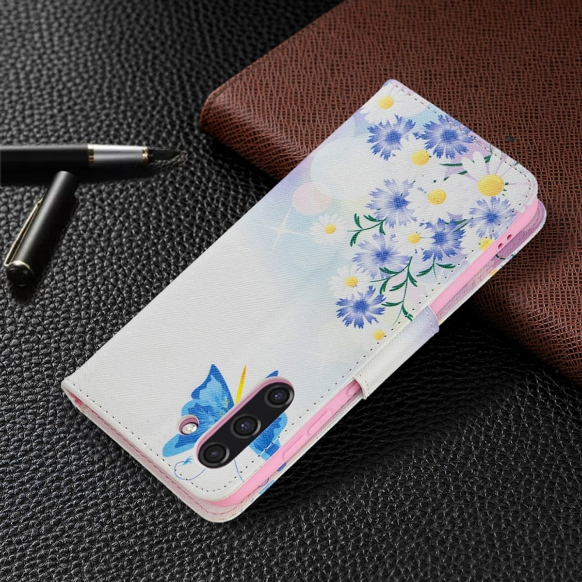 Weiße Handyhülle mit blauem Blumen- und Schmetterlingsdesign. Geöffnet auf dunklem Hintergrund.