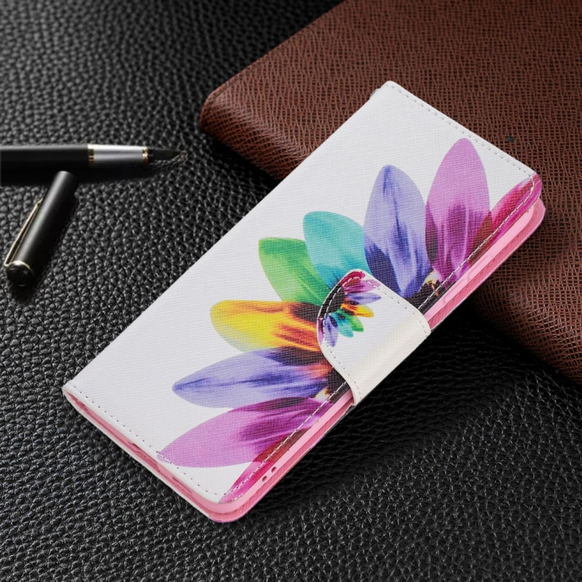Weiße Handyhülle mit bunten Blumen. Stift und brauner Notizblock im Hintergrund.