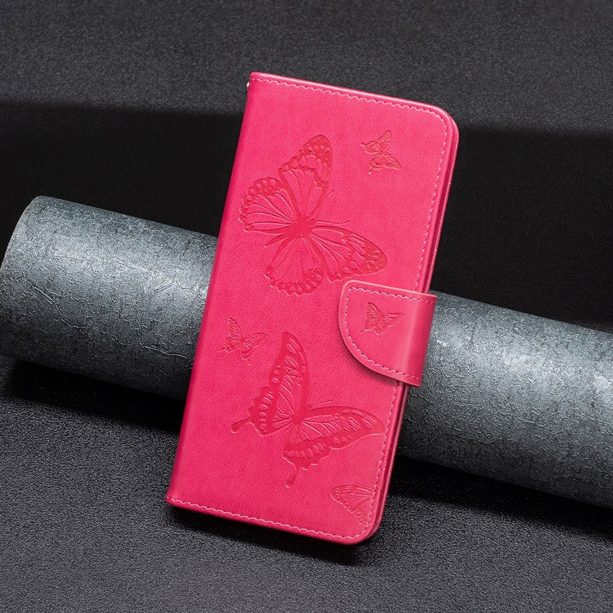 Pinke Handyhülle mit geprägten Schmetterlingen, geschlossen. Dunkler Hintergrund, lederartige Textur.