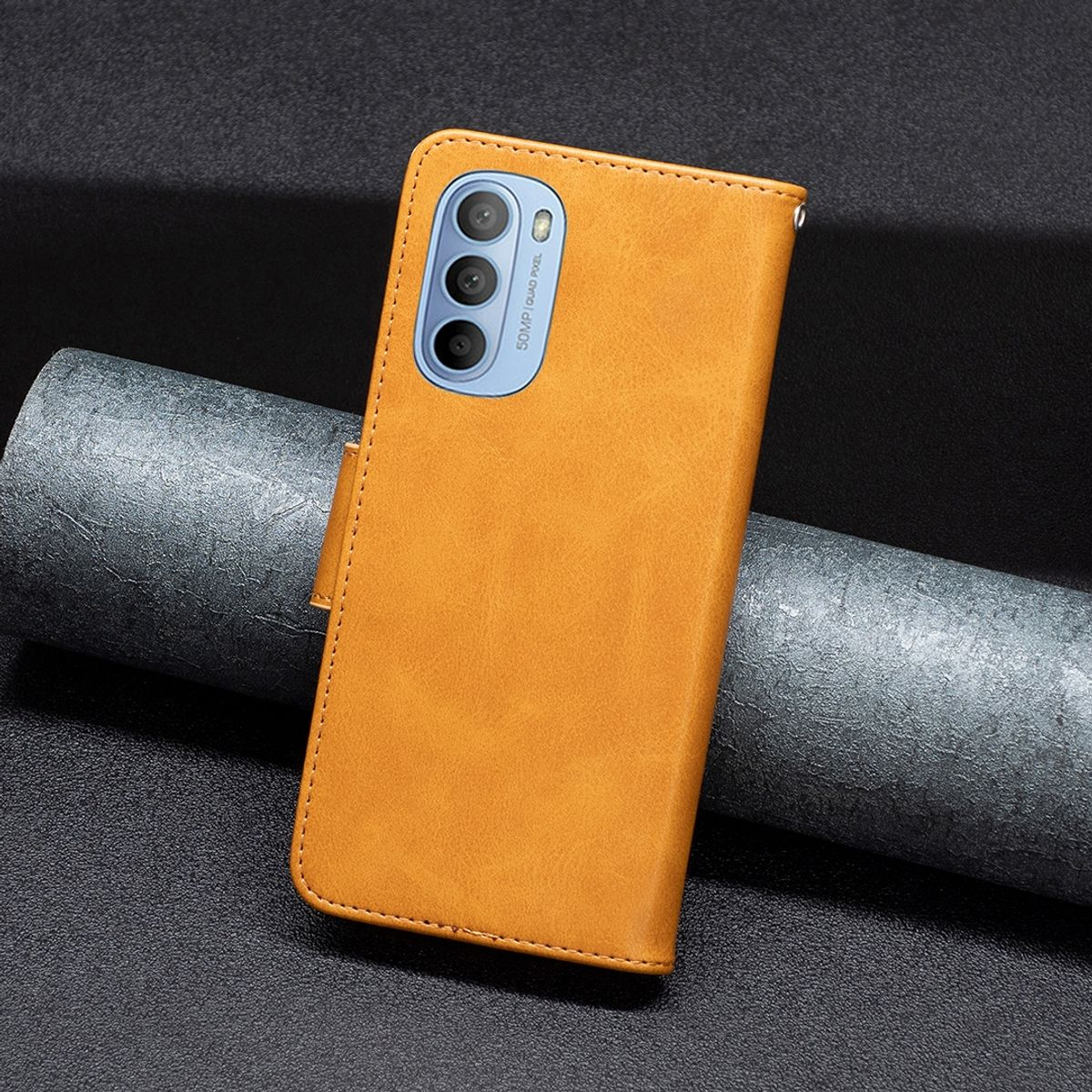 Orangefarbene Handyhülle mit schwarzem Telefon. An grauen Zylinder gelehnt.