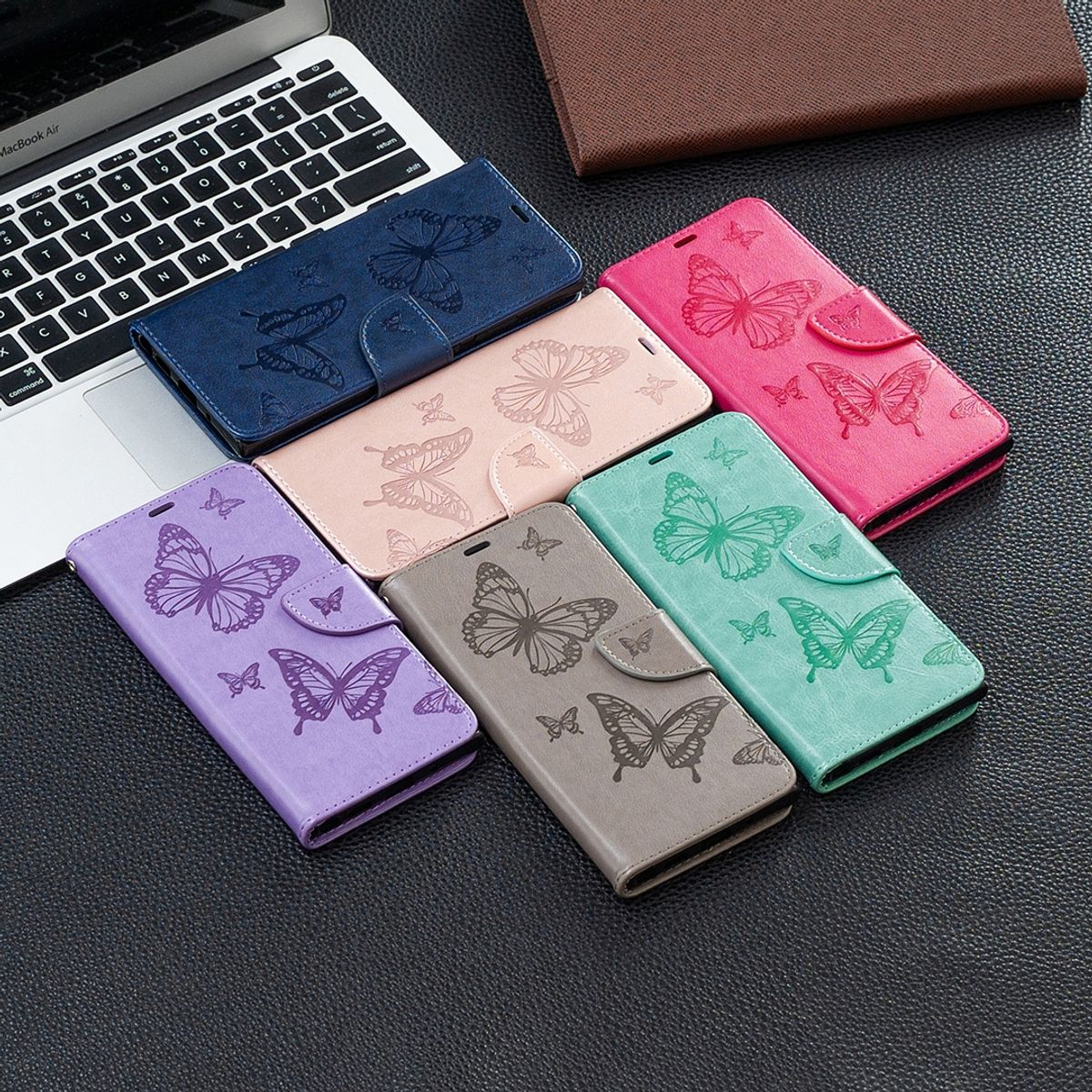 Sortiment an Handyhüllen auf dunkler Oberfläche. Hüllen in Lila, Blau, Pink und Grau, jeweils mit Schmetterling.