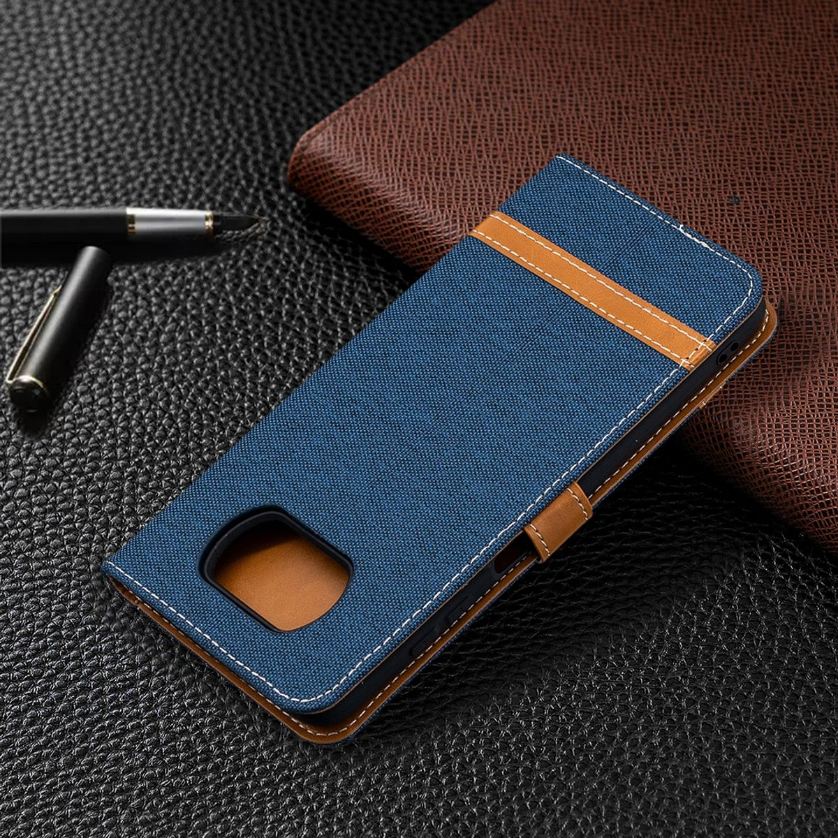 Blaue Handyhülle mit braunem Riemen. Auf schwarzer Lederoberfläche, mit Stift und braunem Etui.