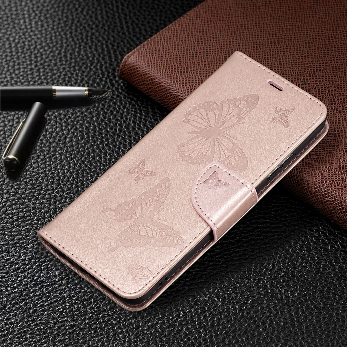 Rosa Handyhülle mit Schmetterlingsdesign, auf strukturierter Oberfläche, mit Stift.