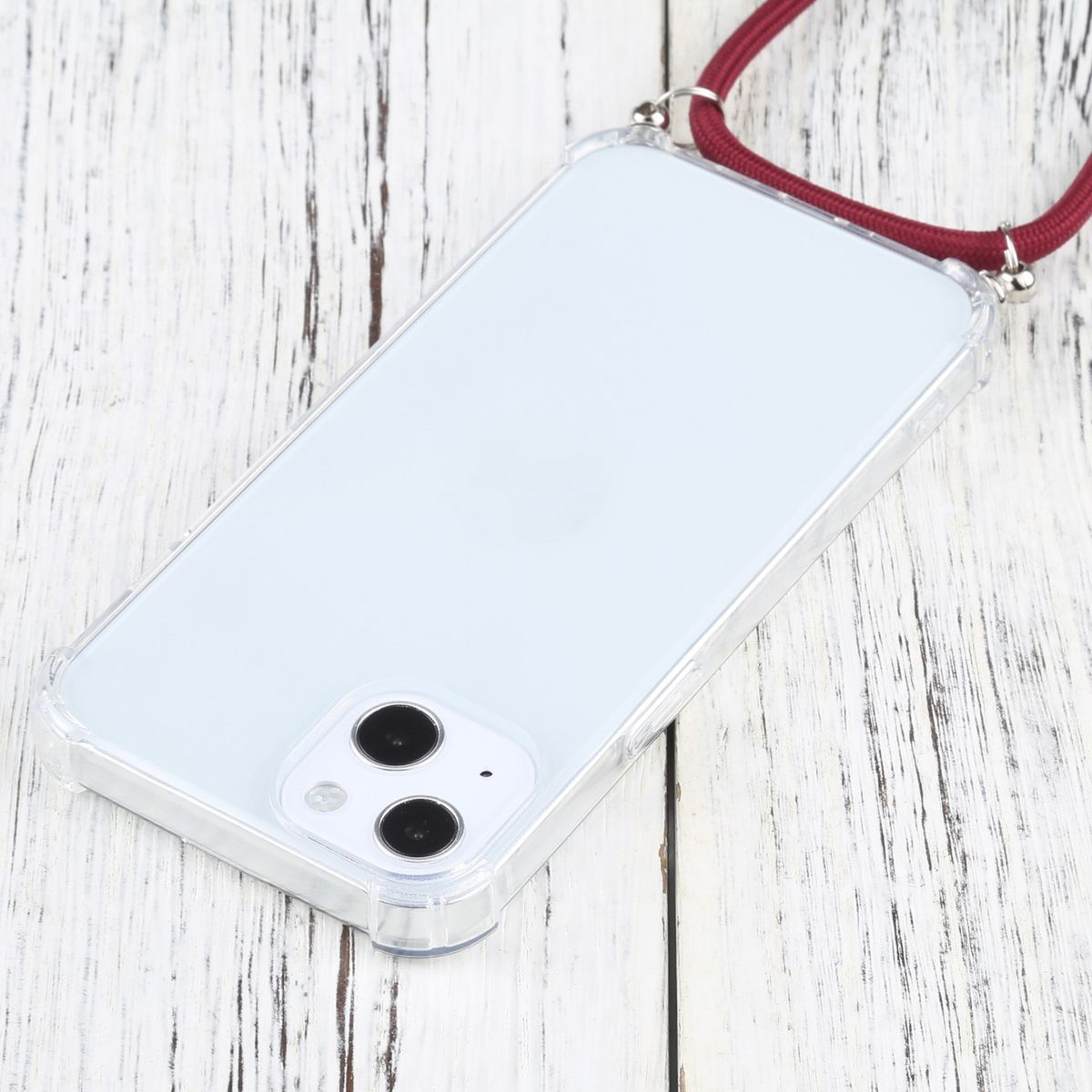Eine transparente Handyhülle mit Telefon und rotem Riemen liegt auf Holz.