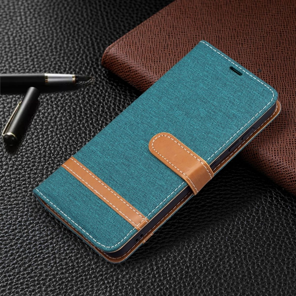 Türkis Handy-Brieftasche. Brauner Riemen mit weißer Naht. Schwarzer Hintergrund. Stift daneben.
