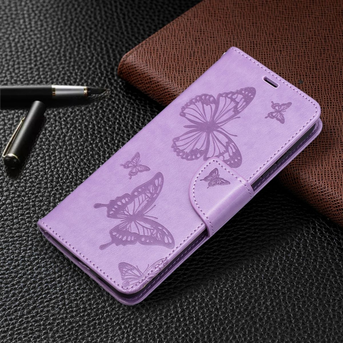 Lila Handyhülle mit Schmetterlingsdesign. Lederstruktur. Enthält einen Stift und ein braunes Lederportemonnaie im Hintergrund.