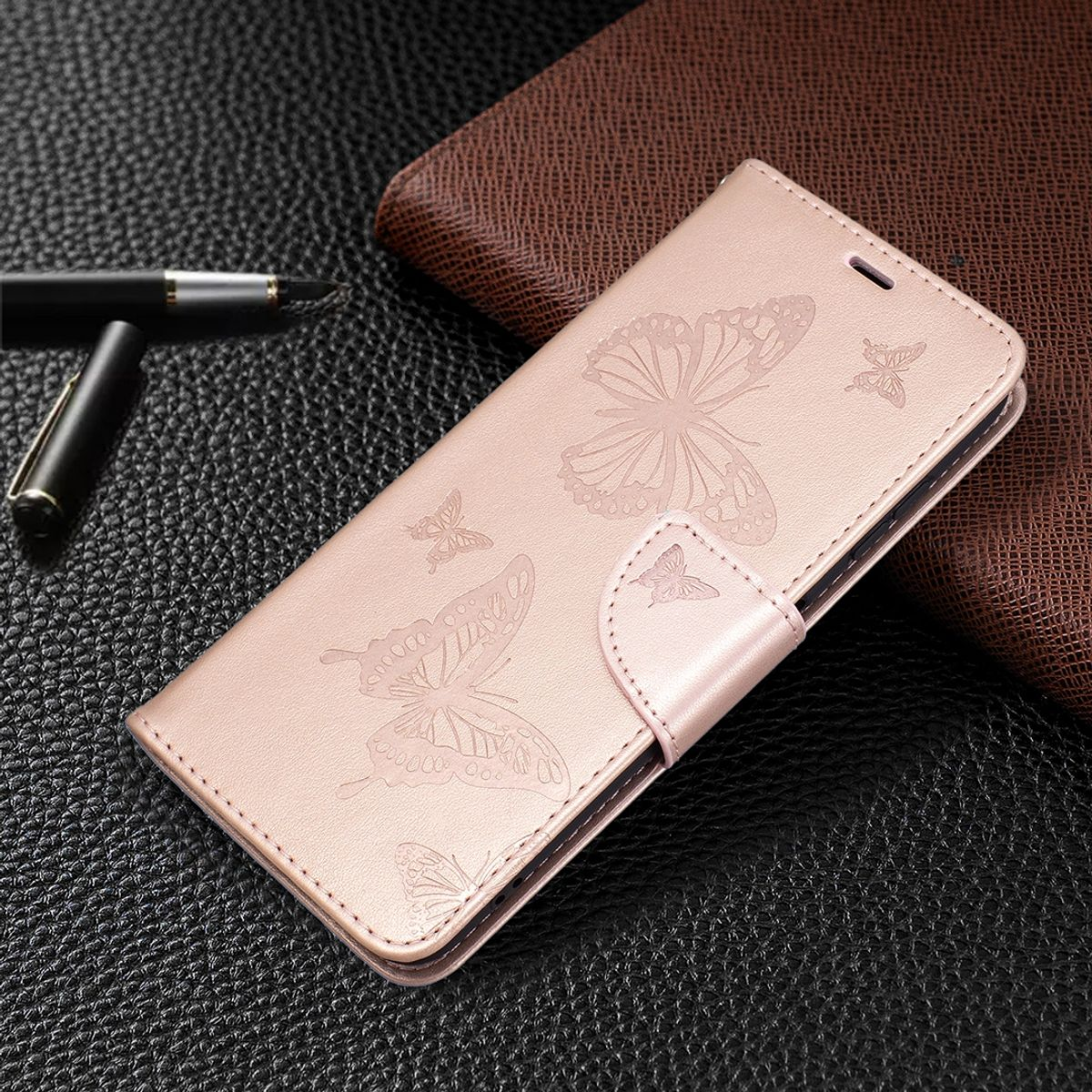 Rosa Handyhülle mit Schmetterlingsdesign, teilweise geöffnet. Ein Stift und eine Geldbörse liegen.