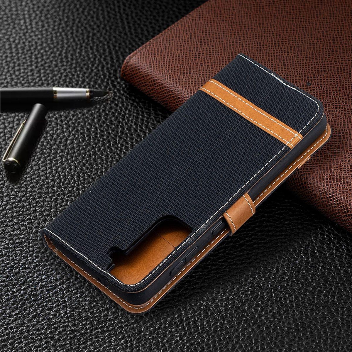 Schwarz-braune Handyhülle mit Telefon, Stift und Notizbuch im Hintergrund.