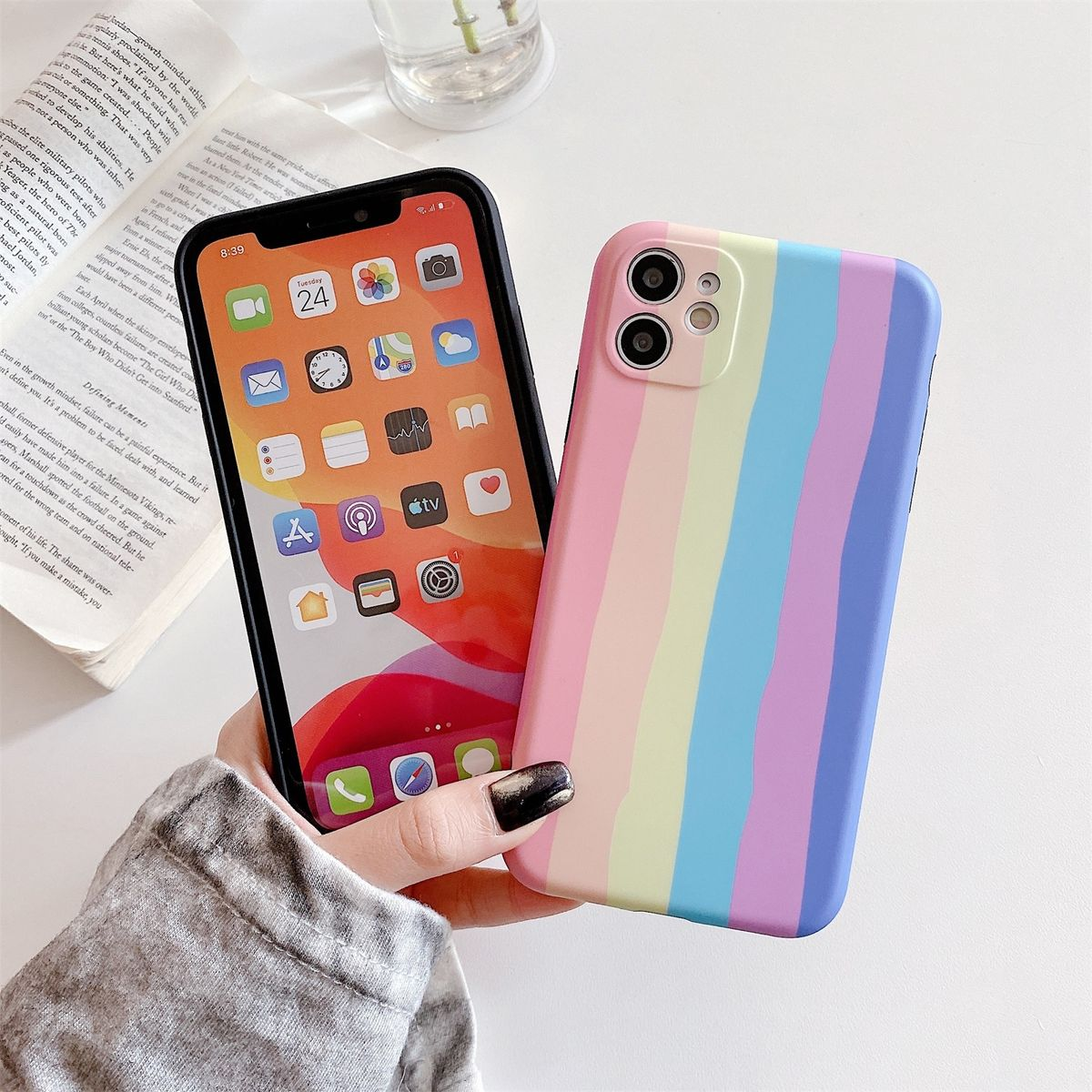 Zwei Telefone auf einem Tisch. Eines mit Regenbogen-Streifen-Hülle, das andere mit Startbildschirm.