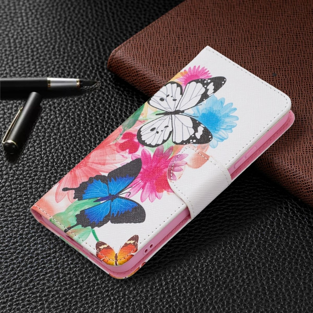 Weiße Handyhülle, offen, mit Schmetterlings- und Blumendesign. Im Hintergrund liegen ein schwarzer Stift und ein braunes Portemonnaie.