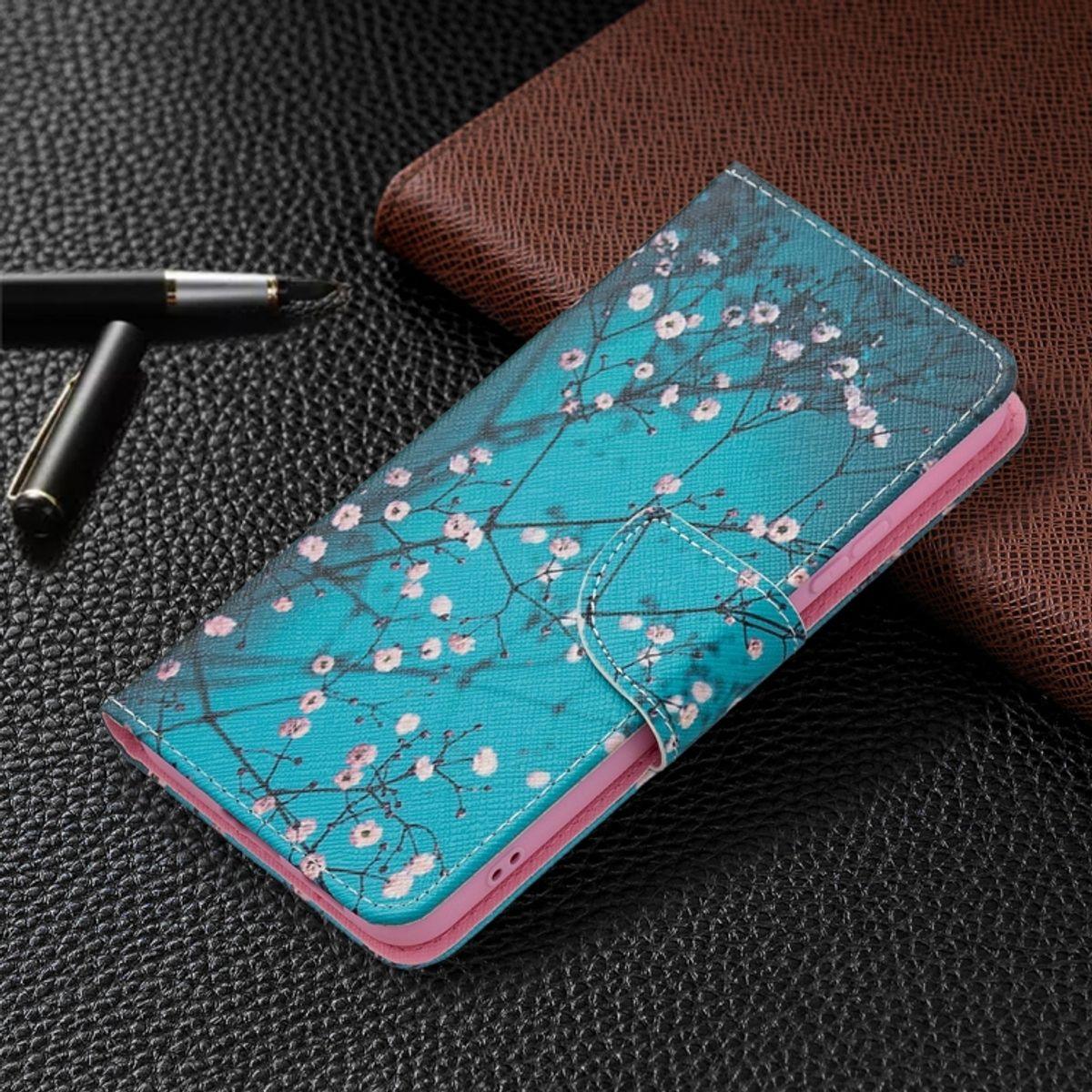 Handyhülle mit floralem Design auf dunkler Oberfläche. Stift in der Nähe. Lederstruktur.