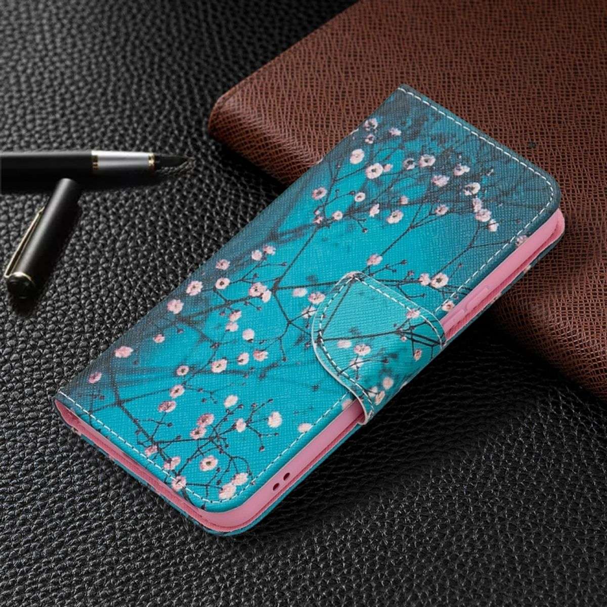 Türkisfarbene Handyhülle mit Blumen und einem rosa Innenraum. Ein Stift ist im Hintergrund.