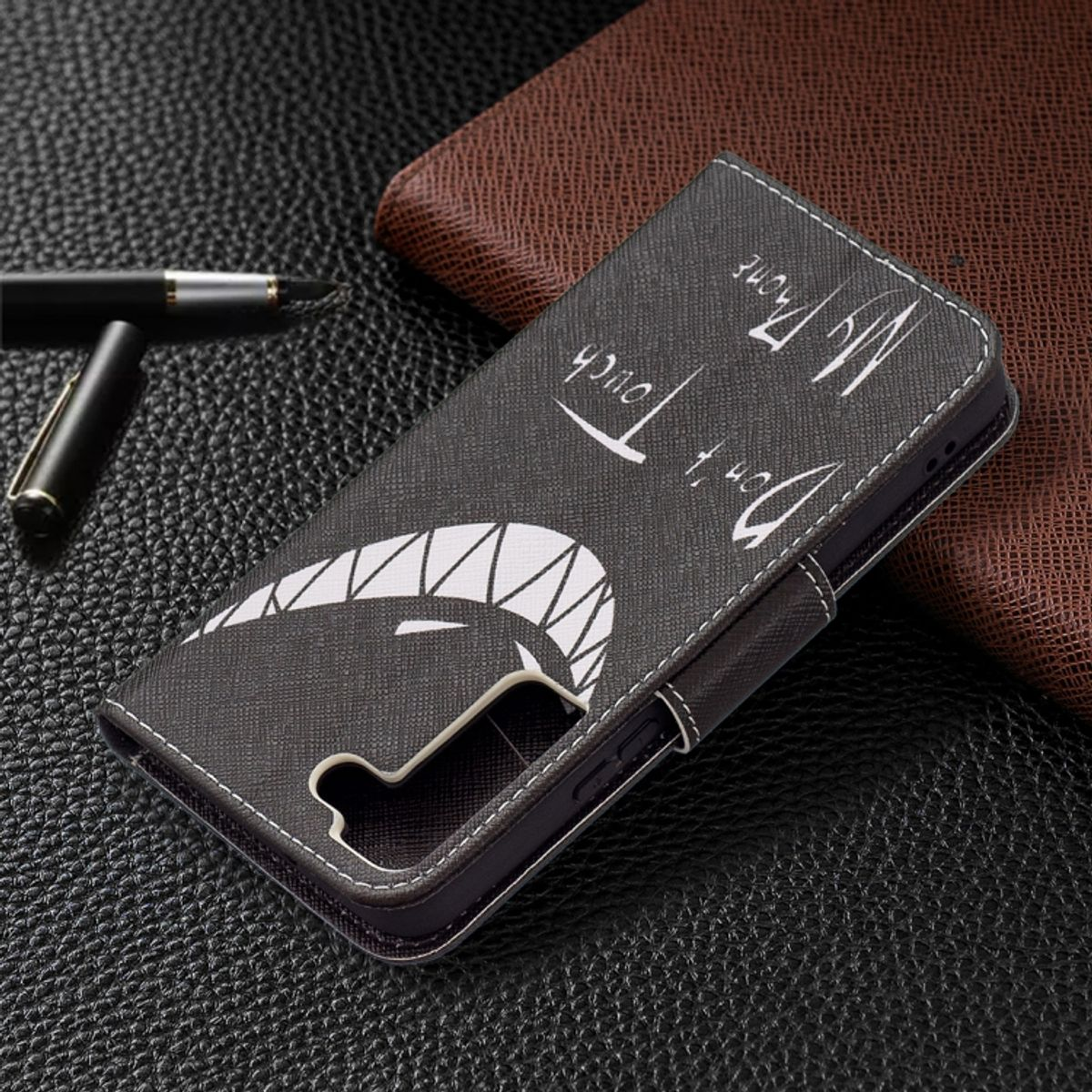 Schwarze Handyhülle mit Design darauf. Text: Berühren Sie nicht mein Telefon. Stift und Geldbörse im Hintergrund.