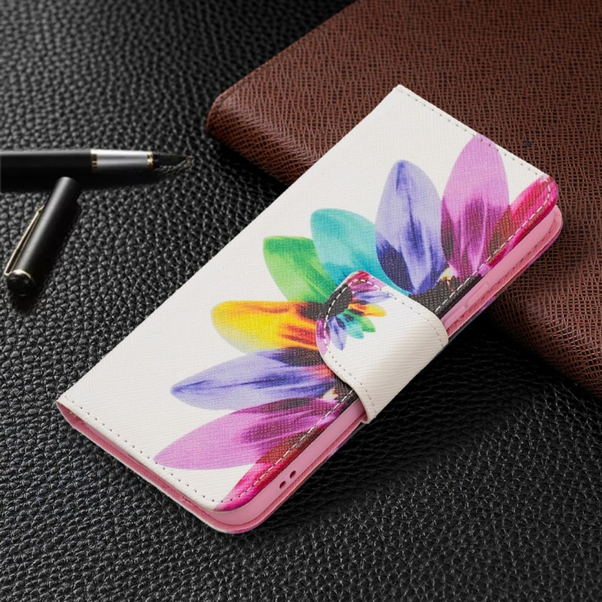 Weiße Handyhülle mit farbenfrohem Blumenmuster. Sie ist offen und liegt auf dunklem Untergrund mit Stift.