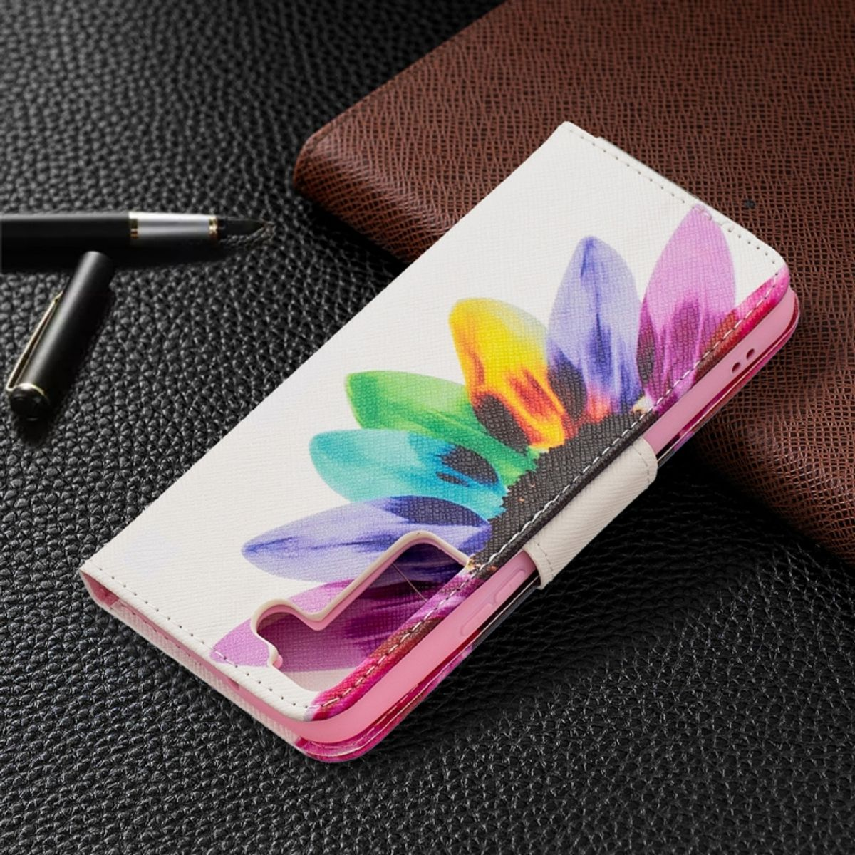 Weiße Handyhülle mit buntem Blumendesign. Braune Geldbörse auf schwarzem Untergrund im Hintergrund.