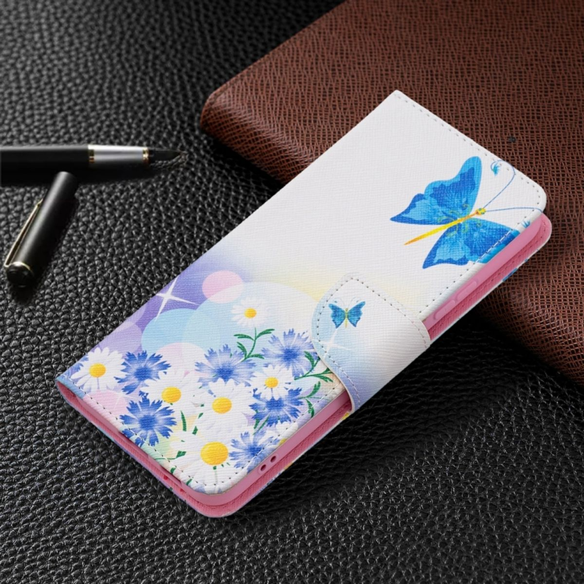 Weiße Handyhülle mit Blumen und einem blauen Schmetterling. Auf schwarzer Lederoberfläche.