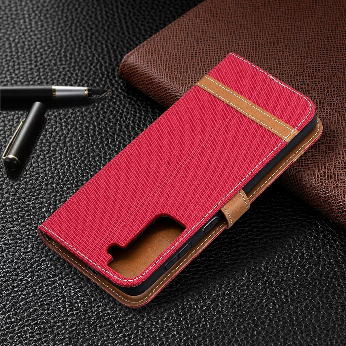 Rote Handyhülle auf strukturierter Oberfläche mit Stift und Notizbuch im Hintergrund.