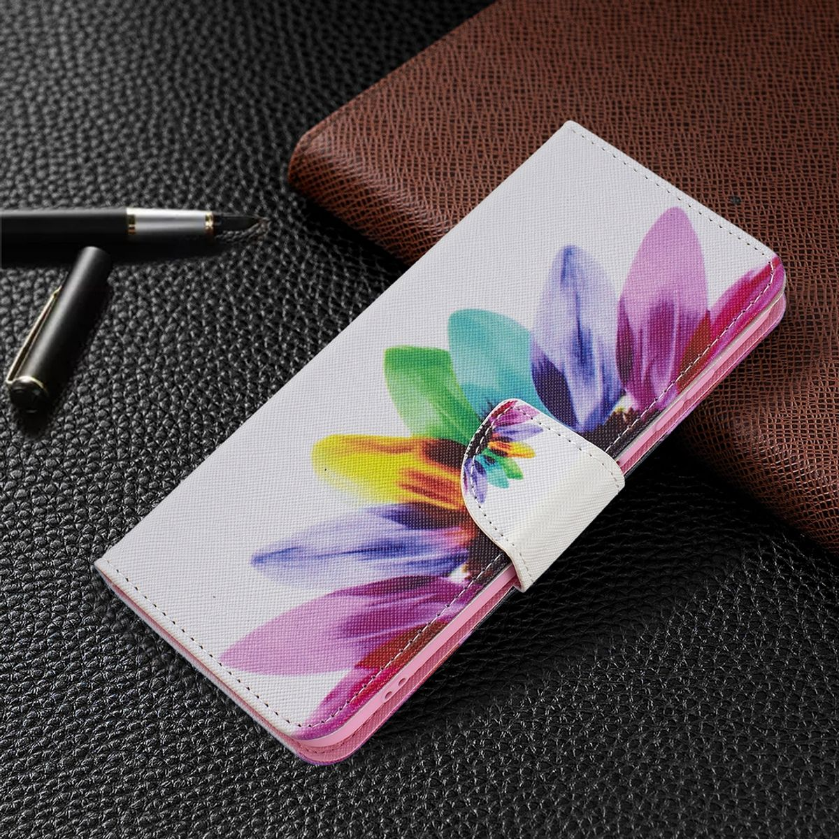 Eine weiße Handyhülle mit einem bunten Blumendesign. Ein Stift und dunkler Untergrund im Hintergrund.