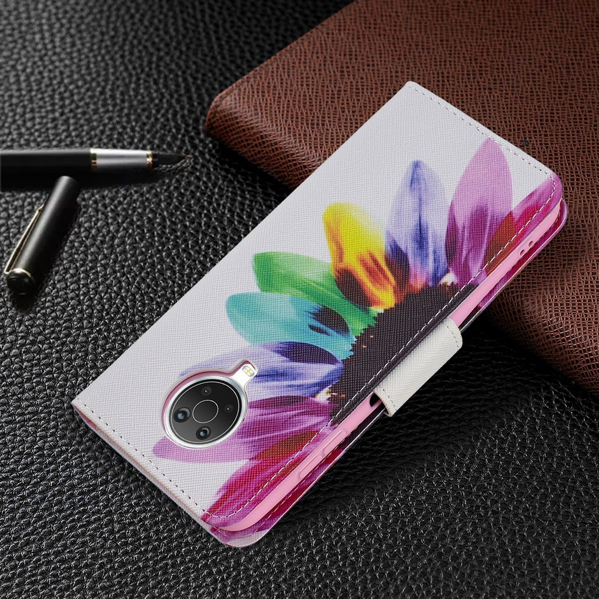 Geöffnete weiße Handyhülle mit buntem Blumendesign. Auf schwarzem Leder, mit Stift obenauf.