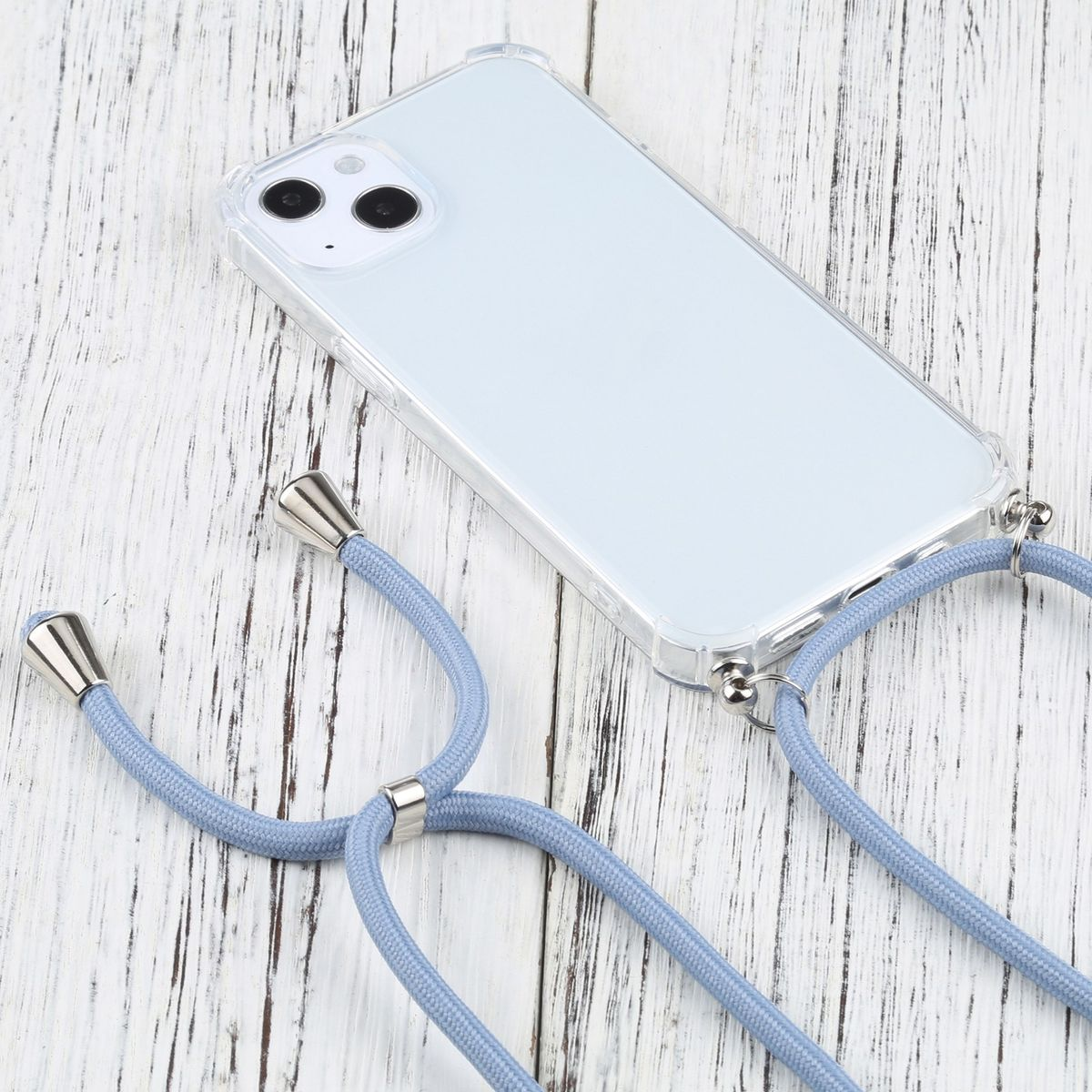 Transparente Handyhülle an hellblauer Kordel. Silberne Akzente. Telefon sichtbar, auf weißer Holzoberfläche.