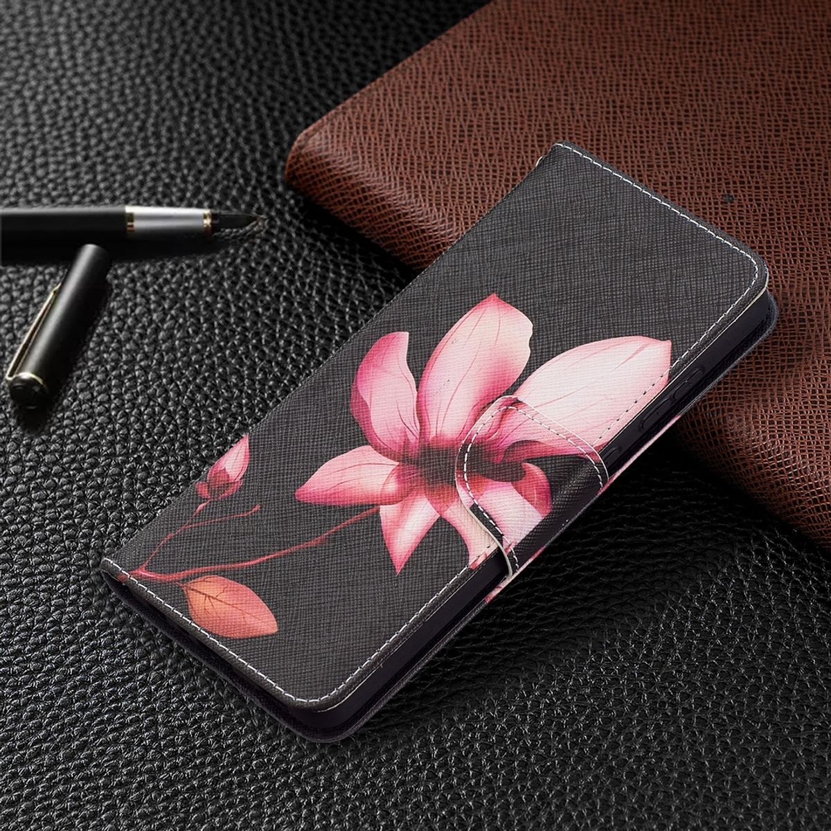 Schwarze Handyhülle mit Blumendesign und weißen Nähten. Sie liegt auf einer strukturierten Oberfläche.