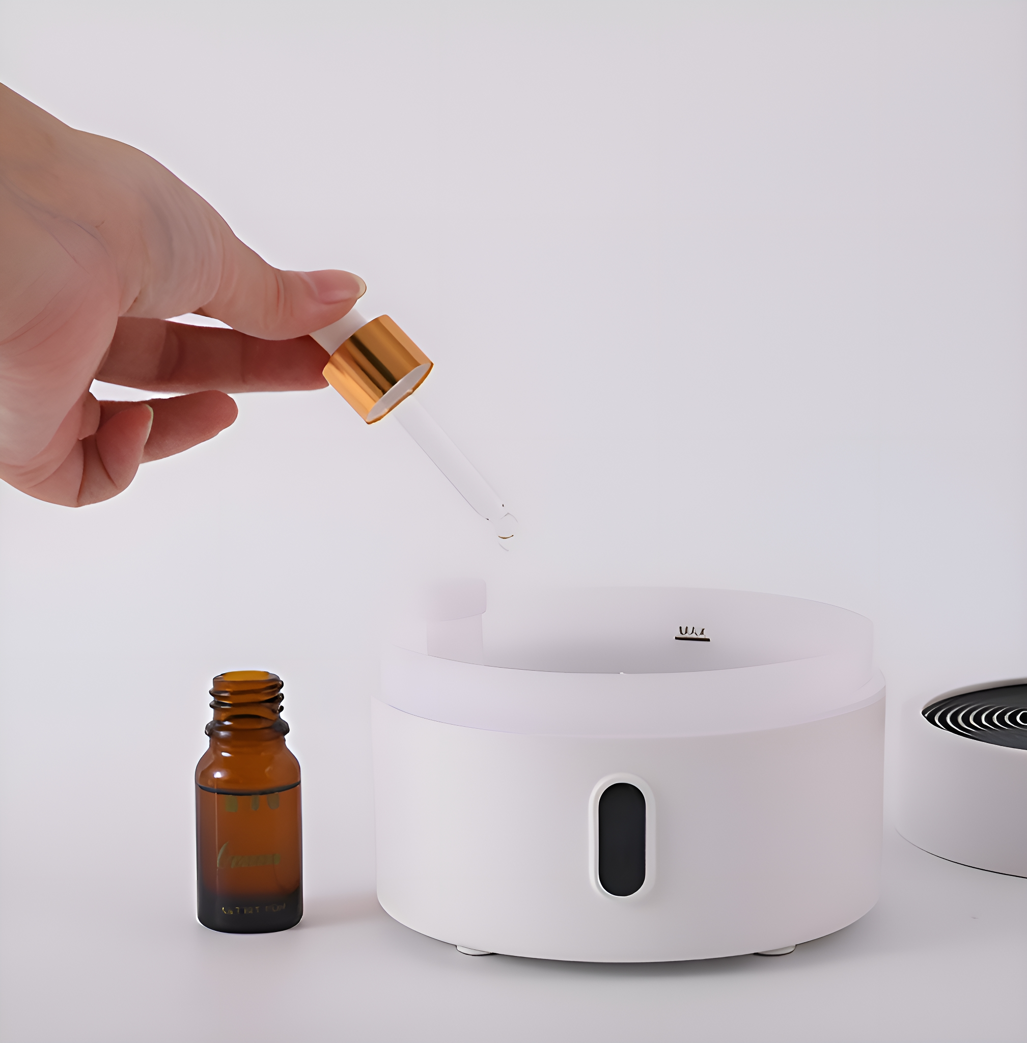 Eine Hand, die eine Pipette über einem weißen Diffusor hält, mit einer braunen Ölflasche.