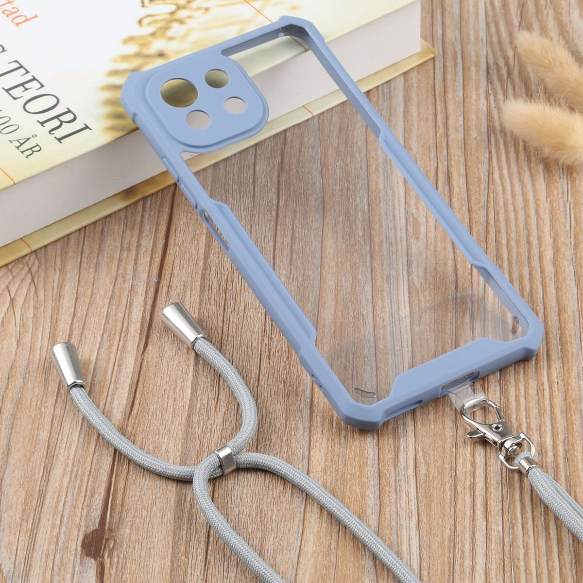 Hellblaue Handyhülle mit Lanyard, neben Buch und Pflanzen.