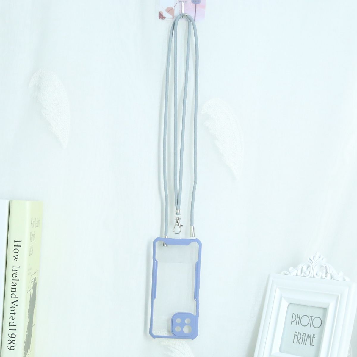 Handyhülle mit Lanyard. Die Hülle ist transparent mit blauem Rand. Hängt an weißer Wand.