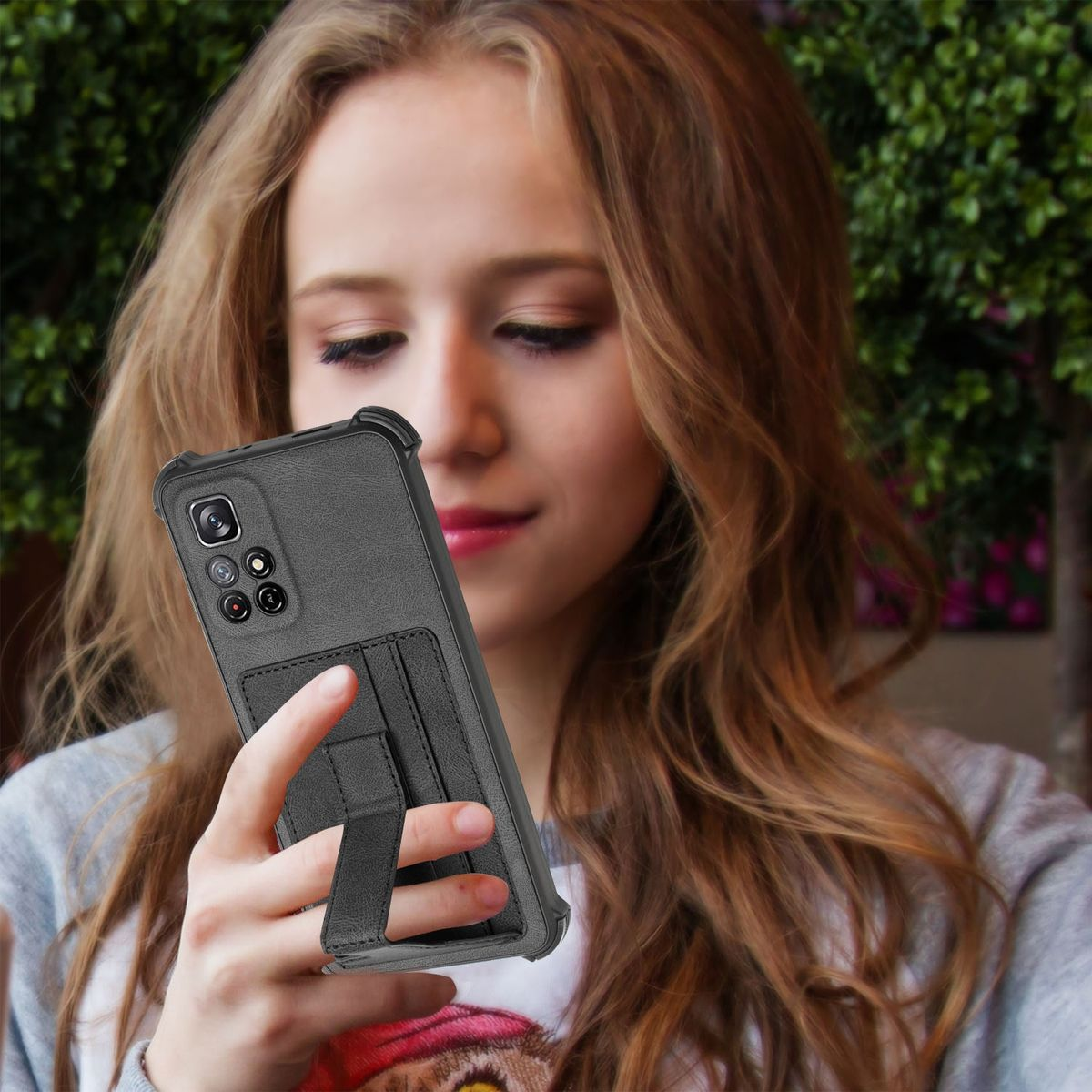 Eine Frau hält ein schwarzes Telefon in einer Hülle mit einem Ständer. Der Hintergrund ist eine verschwommene Szene im Freien.