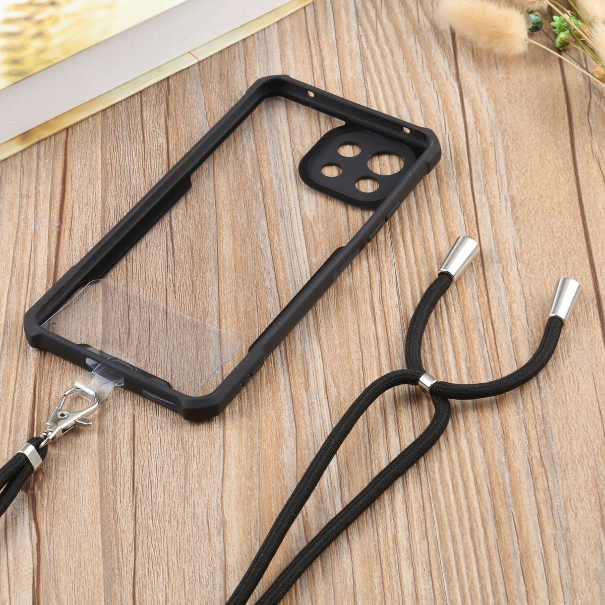 Eine schwarze Handyhülle mit Lanyard und silbernem Verschluss auf einem Holztisch.