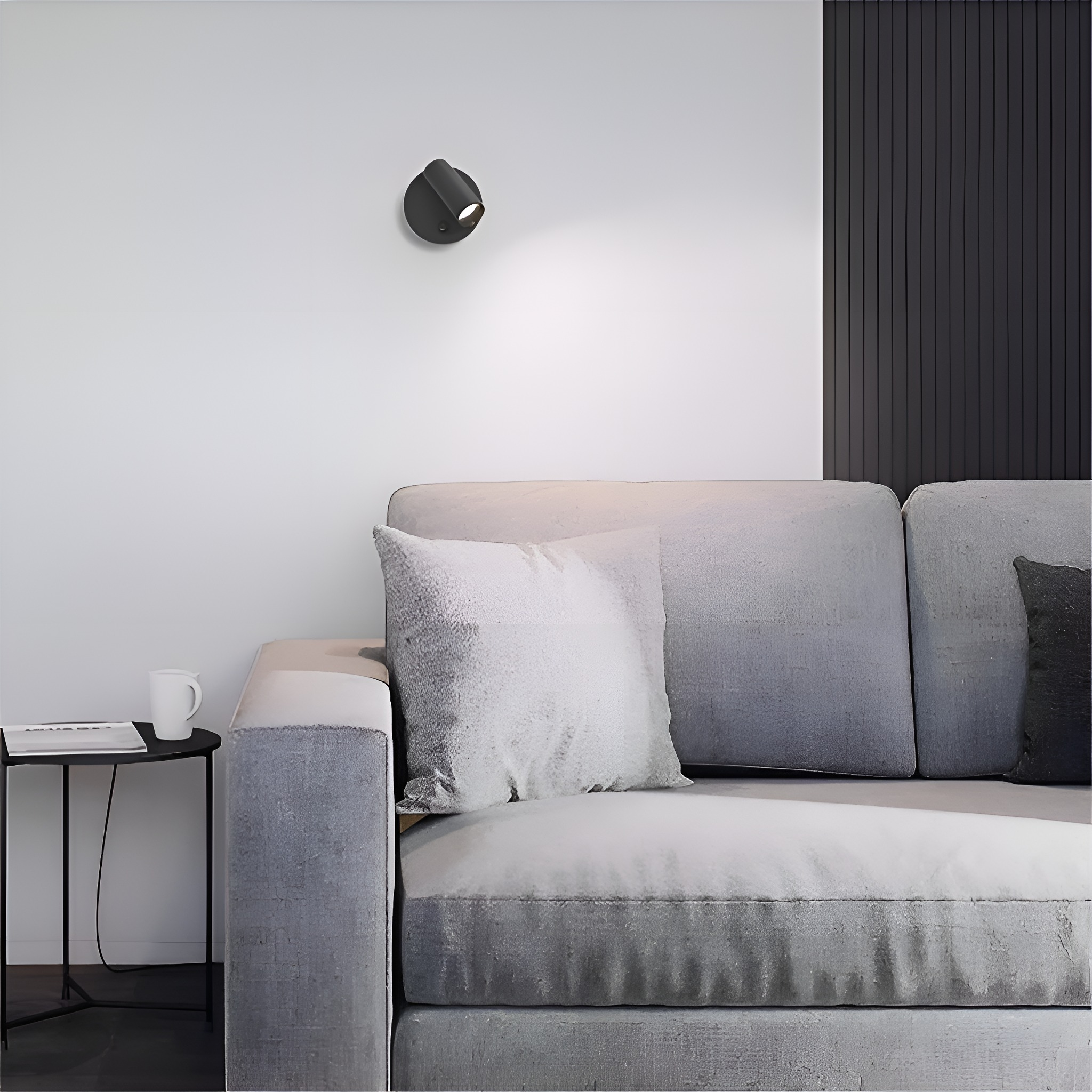 Ein schwarzer, an der Wand montierter Scheinwerfer, der ein graues Sofa mit einem weißen Kissen beleuchtet.