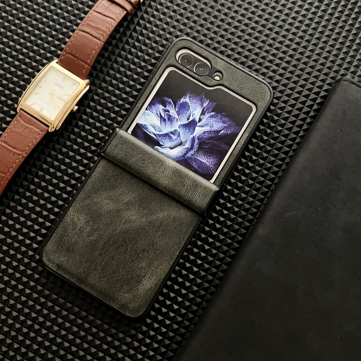 Telefon in einer dunkelgrauen Hülle. Es gibt eine Uhr und eine schwarze Brieftasche.