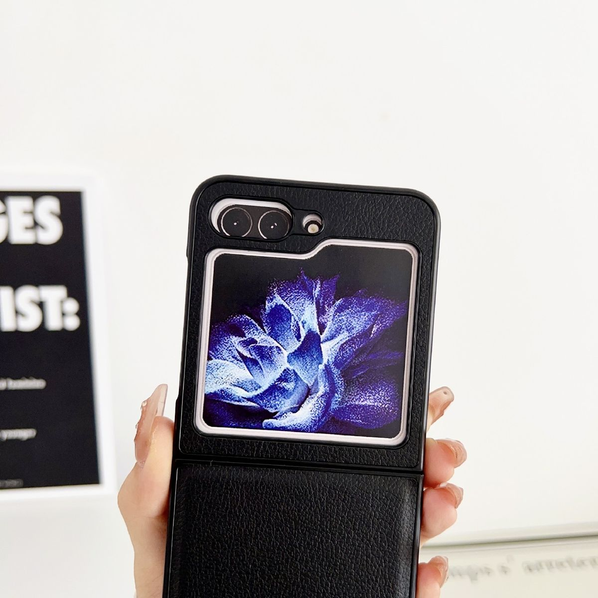 Schwarze Handyhülle mit Blumengrafik. Telefon sichtbar, weißer Hintergrund, Hand hält das Telefon.