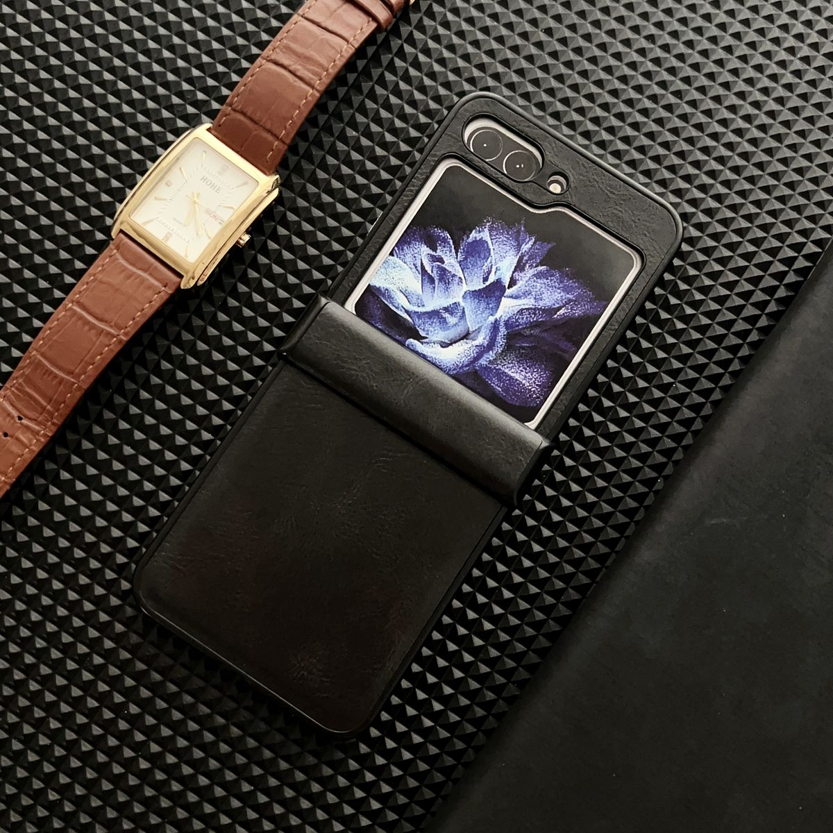 Schwarze Handyhülle mit einer Uhr daneben. Der Telefonbildschirm zeigt ein blaues Blumenmuster.