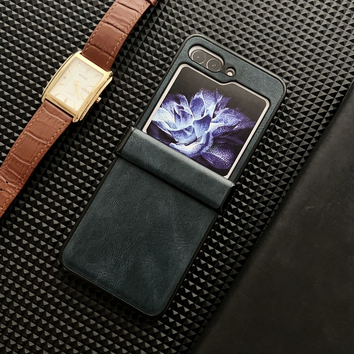 Ein Telefon in einer faltbaren Hülle neben einer Uhr auf einer strukturierten Oberfläche.