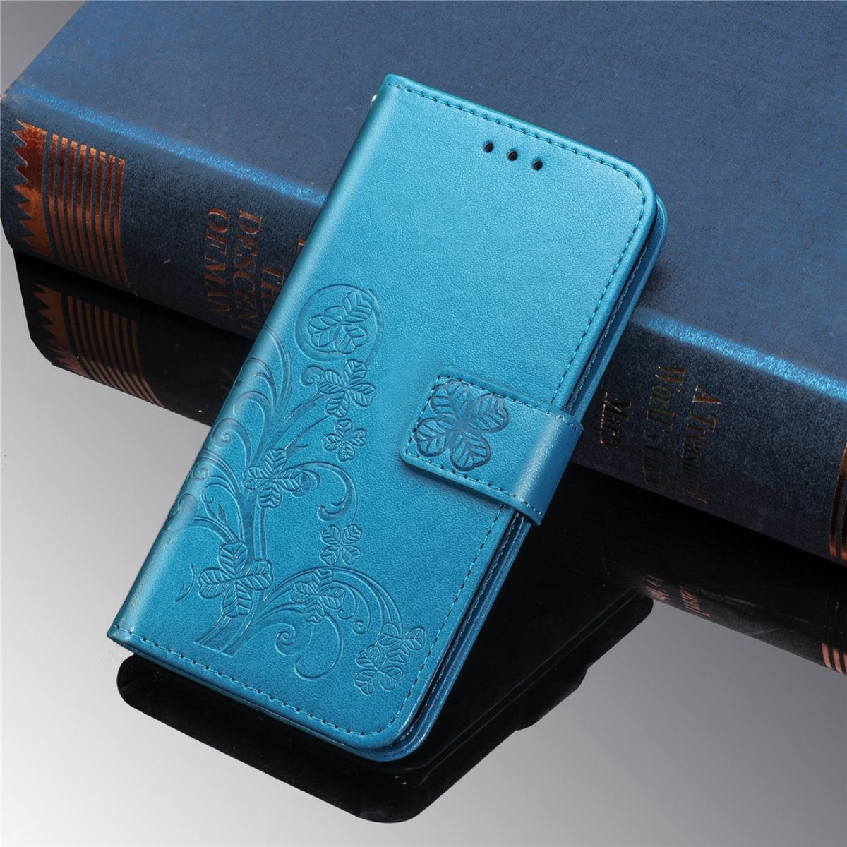 Eine blaue Leder-Handyhülle mit floraler Prägung. Die Hülle ist auf einem dunkelblauen Buch geöffnet.