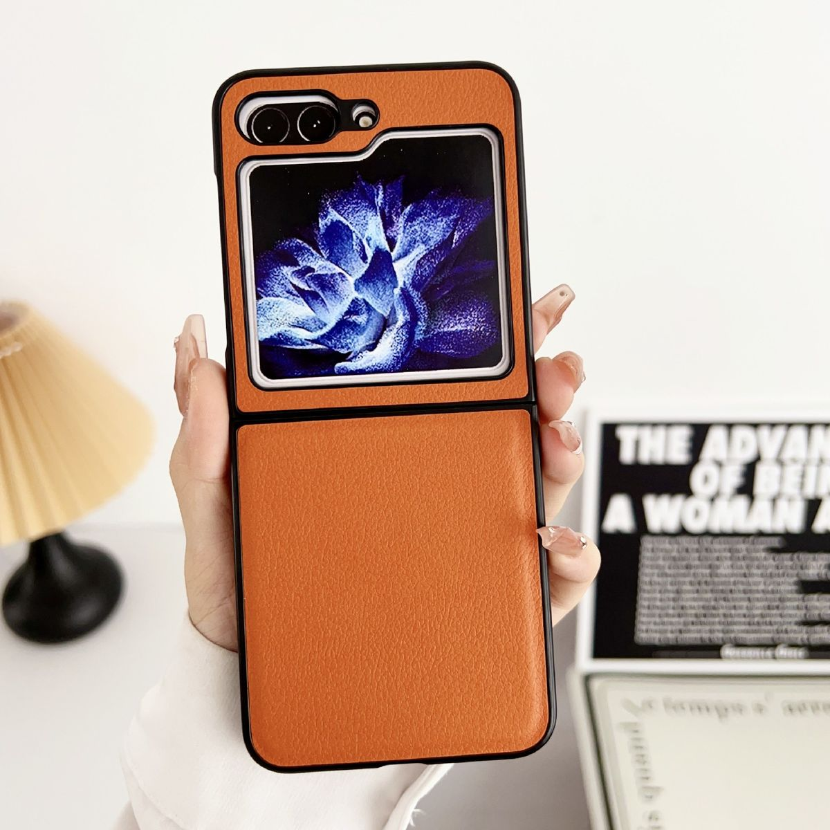 Geöffnete orangefarbene Handyhülle, die einen Telefonbildschirm mit blauem Blumendesign zeigt. In der Hand gehalten.