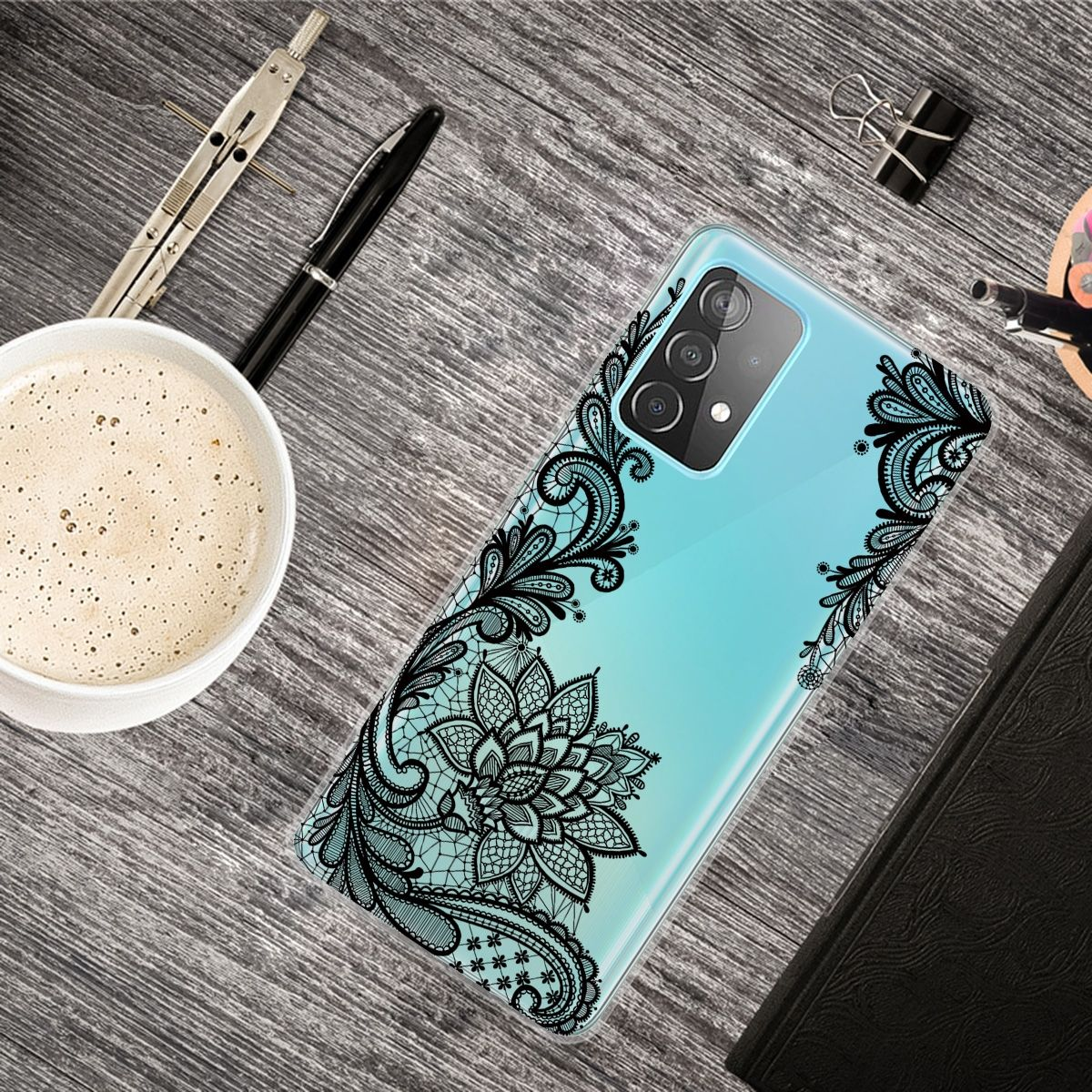 Handyhülle mit Spitzendesign, Stifte, Kaffee und andere Gegenstände auf Holzoberfläche.