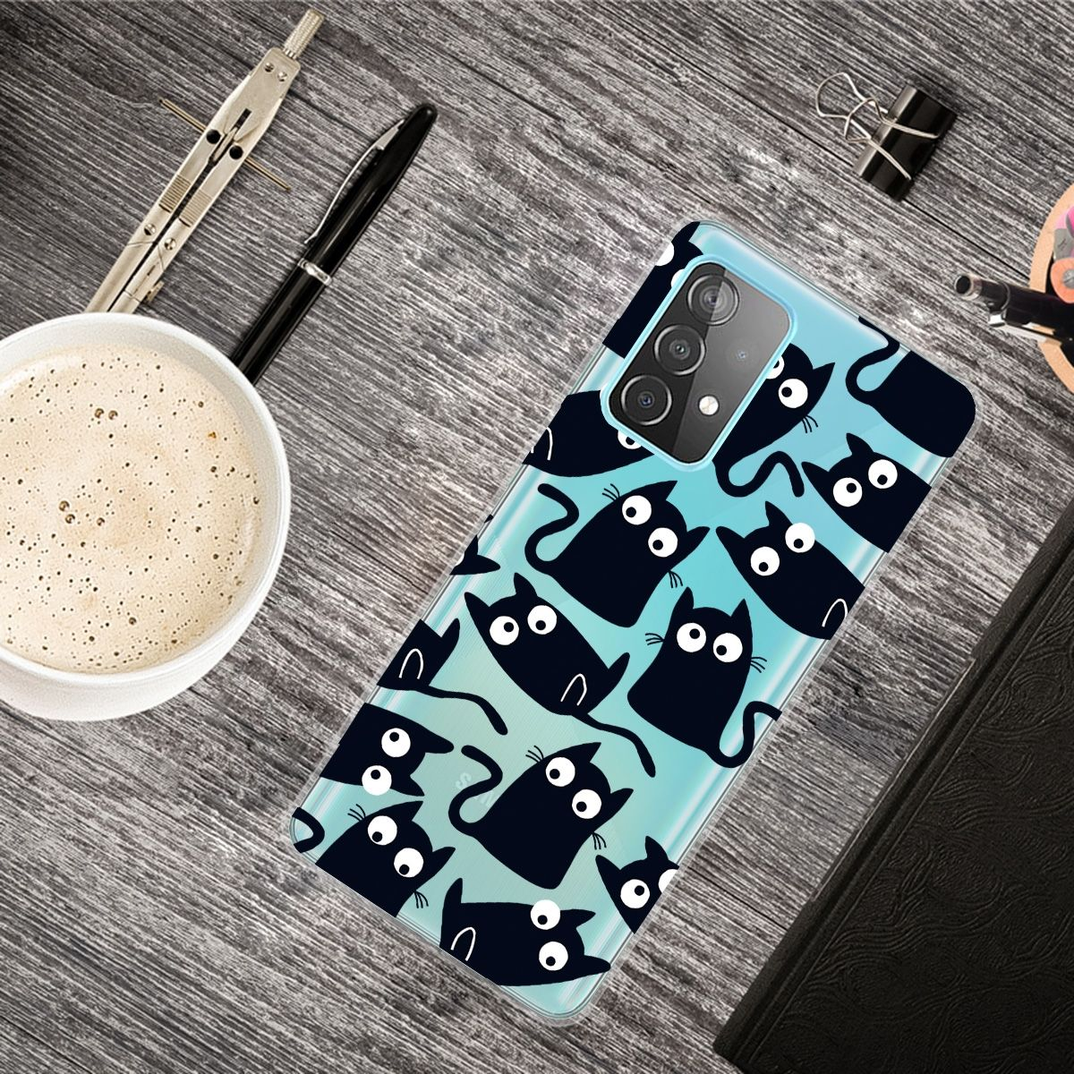 Eine Handyhülle mit Katzenmuster auf Holzoberfläche mit Kaffeetasse und Stiften.