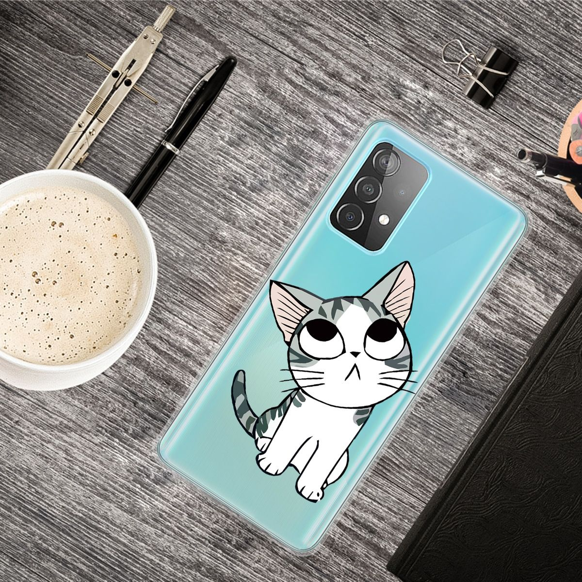 Nahaufnahme einer Handyhülle mit Katzendesign auf einem Holzschreibtisch. Andere Gegenstände: Stift, Kaffee und Buch.