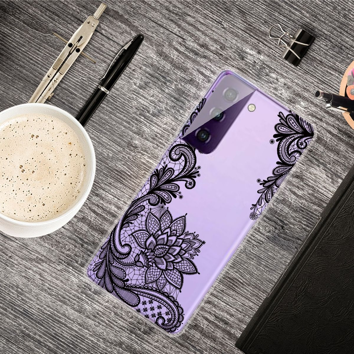 Handyhülle mit helllila Hintergrund und schwarzem Spitzen-Blumendesign. Kaffee und Zubehör sind sichtbar.