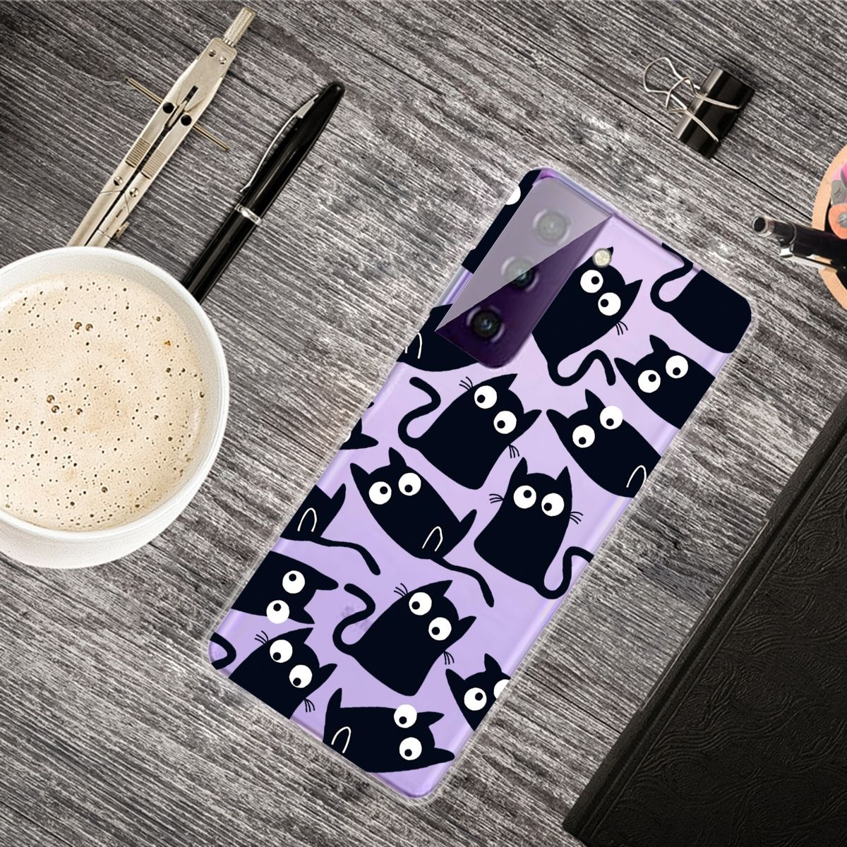 Eine Handyhülle mit schwarzem Katzendesign liegt auf einer Holzoberfläche mit Kaffee und Schreibwaren.