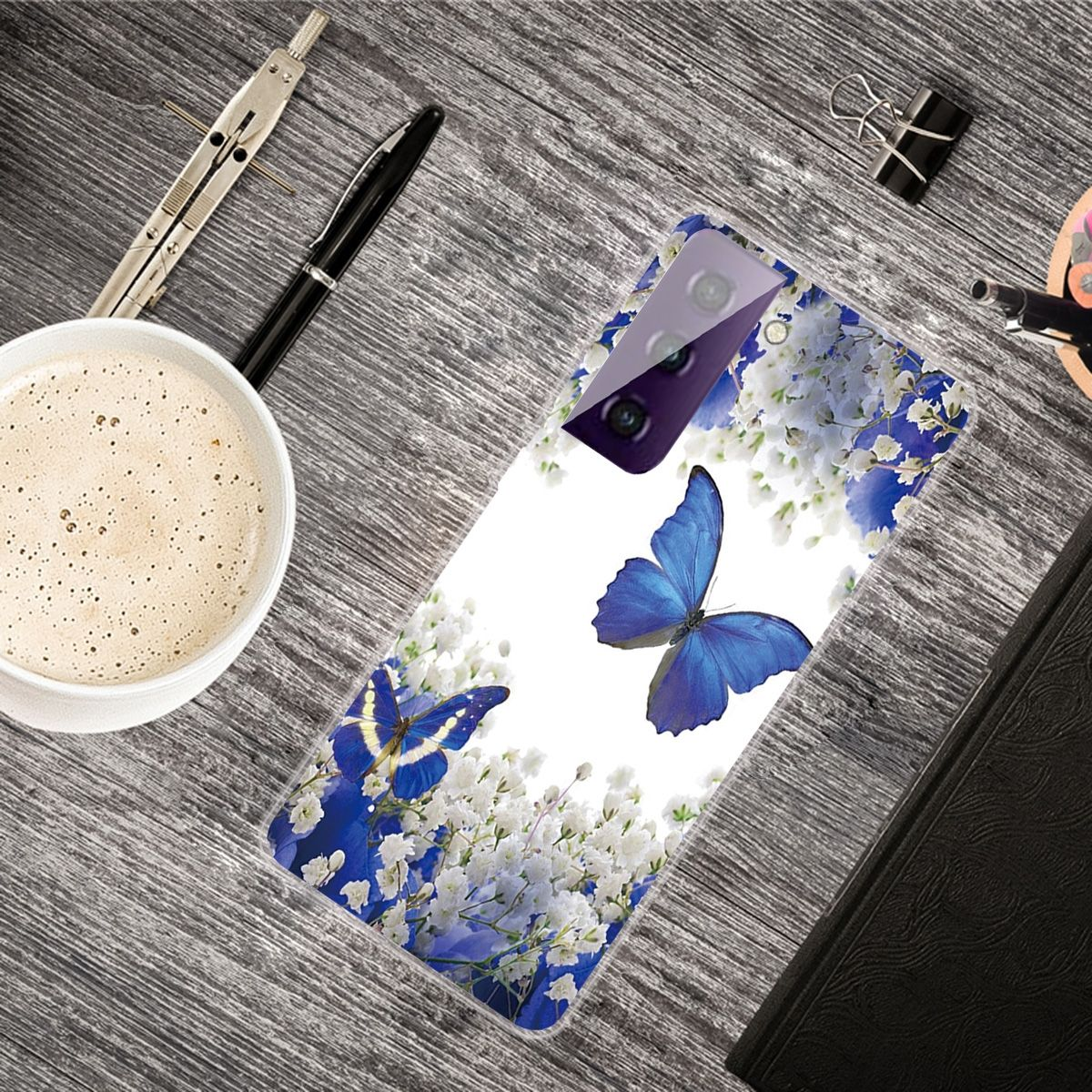 Handyhülle mit blauem Schmetterlingsdesign auf einem Holztisch, mit Kaffee und Stift.